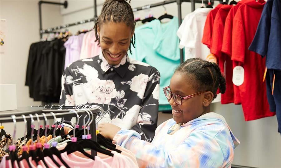 Patrick Woodyard helps Lauryn Silmon find the perfect fit. They laugh and smile while looking through a rack of clothes.
